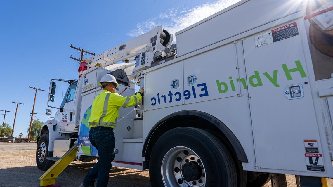 A team member stands next to one of SDG&E's hybrid electric fleet trucks